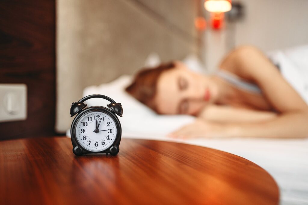 Black alarm clock with woman sleeping on bed on background